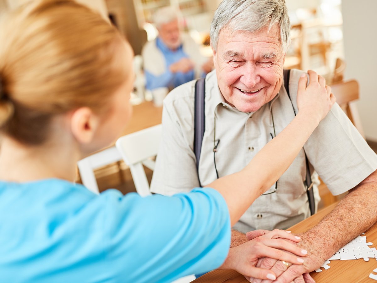 Senior adult day care participant interacting with staff while working on a puzzle